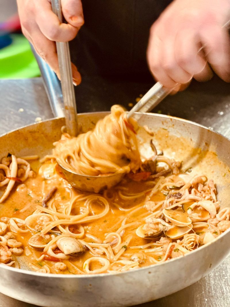 Chef preparing fresh seafood linguine with clams, squid, and shrimp